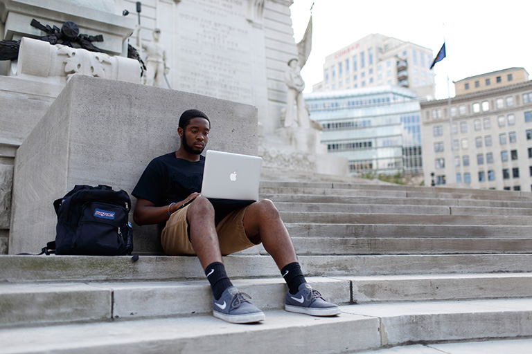 Male student sitting outside on his laptop