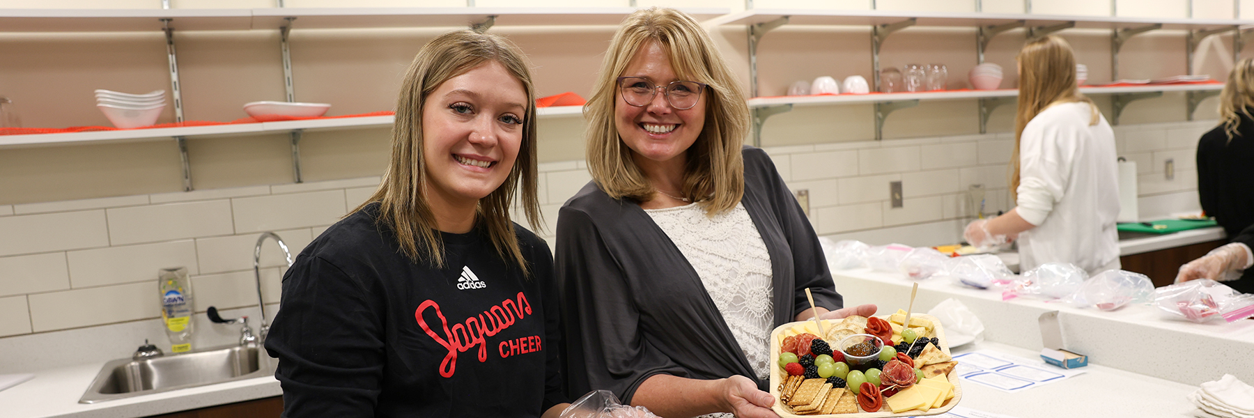 Two people pose in the teaching kitchen with a charcuterie board