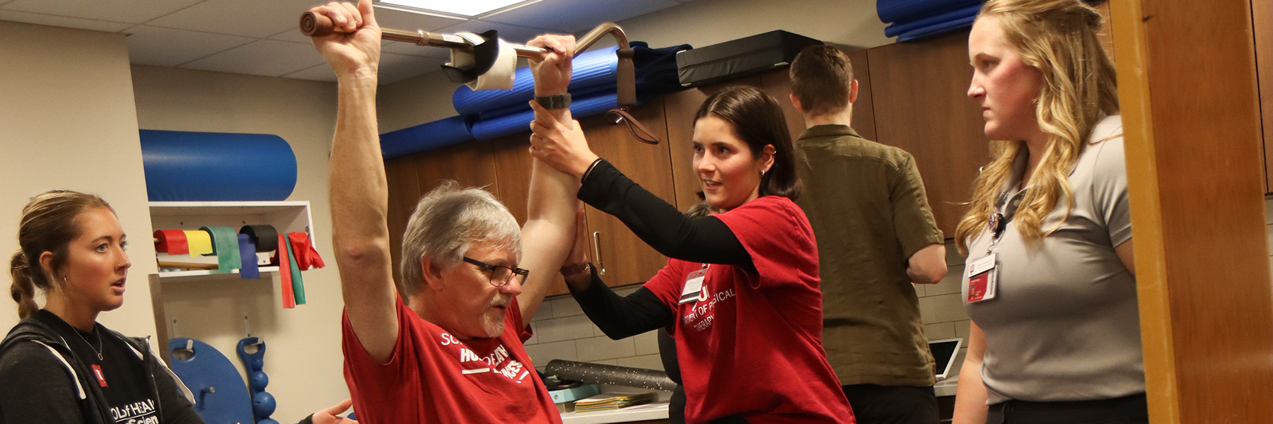 3 PT students helping client lift cane above his head