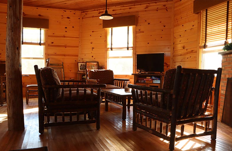 Oversized wooden chairs seen around a table inside a wood paneled cabin-like room.