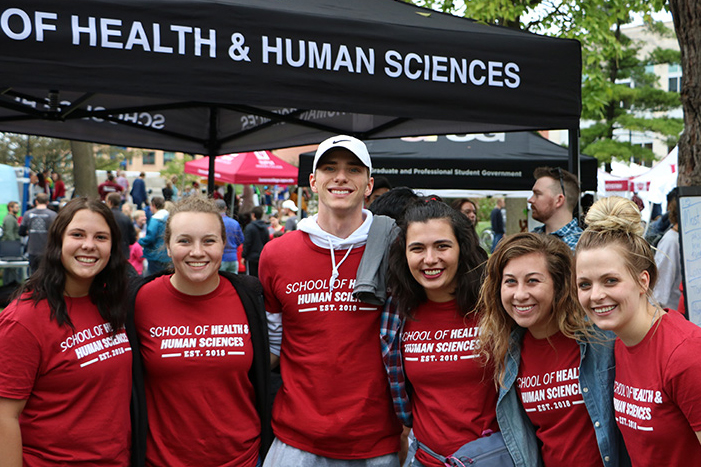 A group of students link arms in front of an SHHS tent at an outdoor event