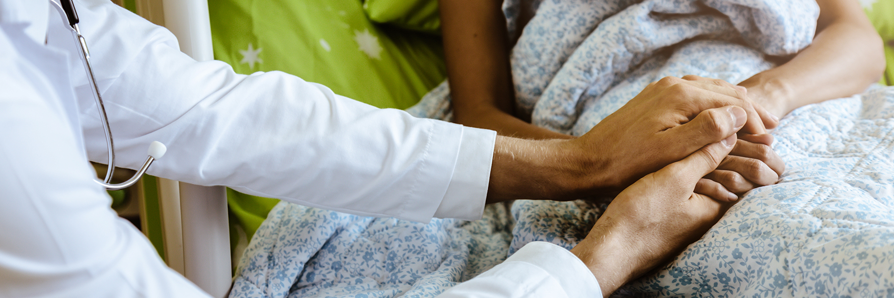 Healthcare provider holds the hand of a patient lying in a hospital bed. 